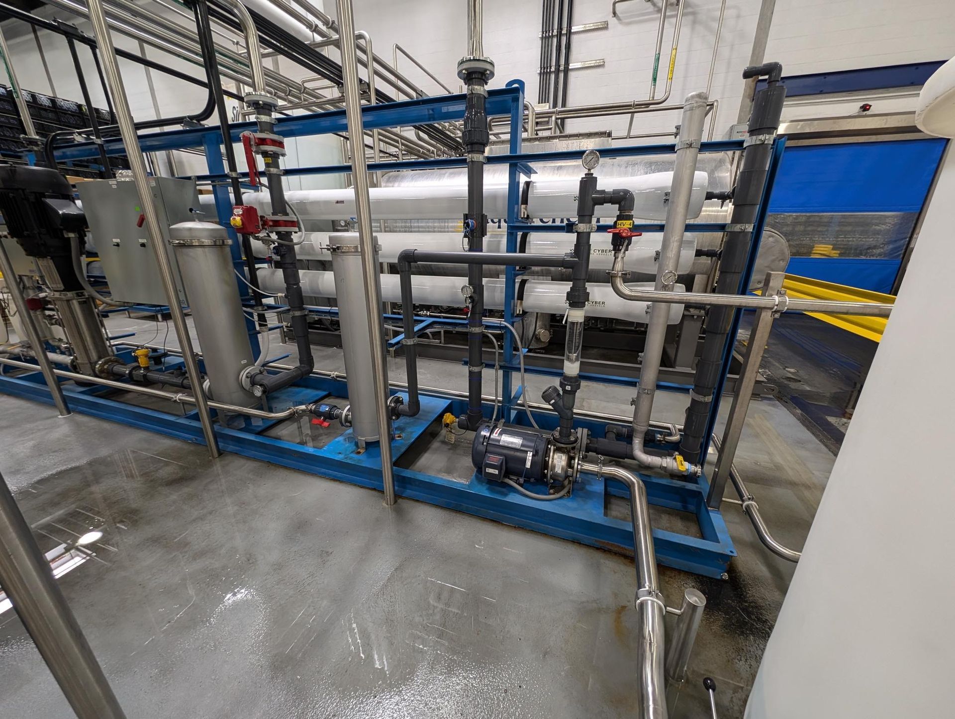 Industrial piping and pump assembly on a blue metal frame in a factory setting