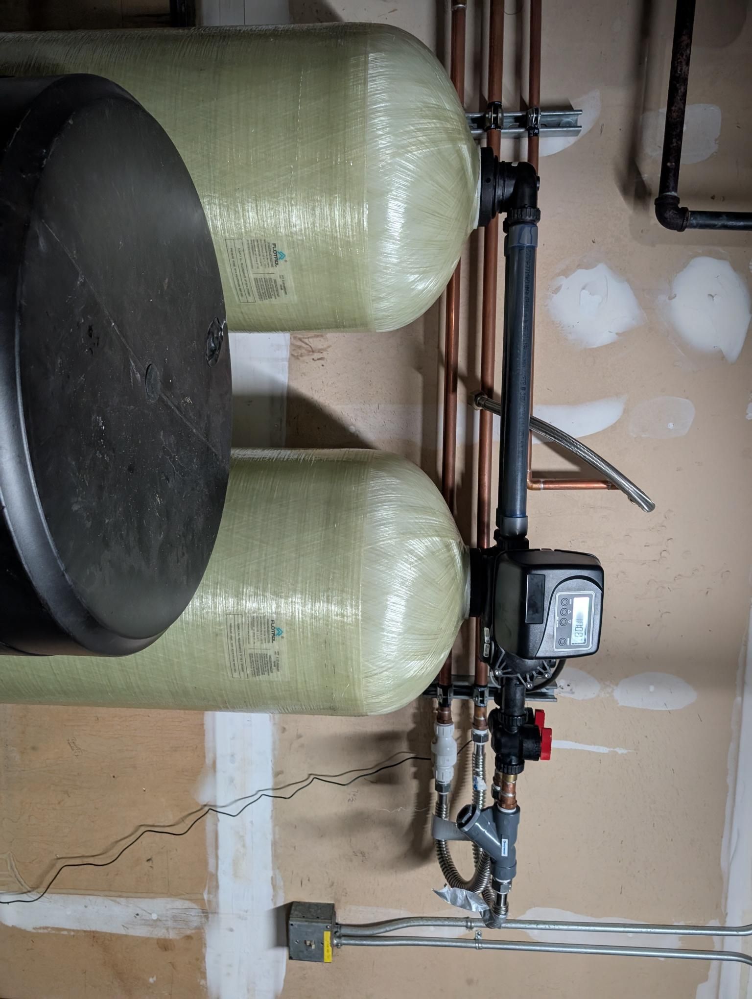 Two green tanks and a black filter tank in a utility room with copper pipes and a control unit.
