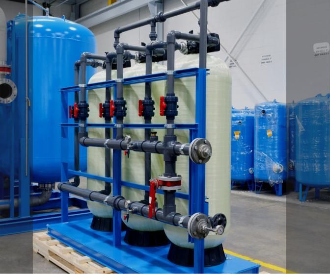 Industrial water filtration system with blue tanks, black pipes, and red valves in a factory setting