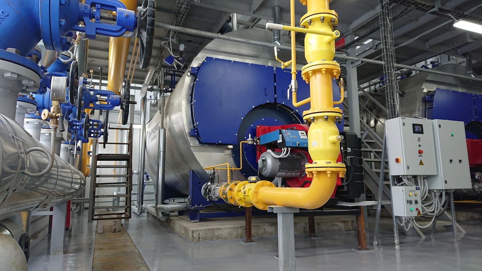 Industrial machinery with large blue tanks and yellow pipes inside a factory facility