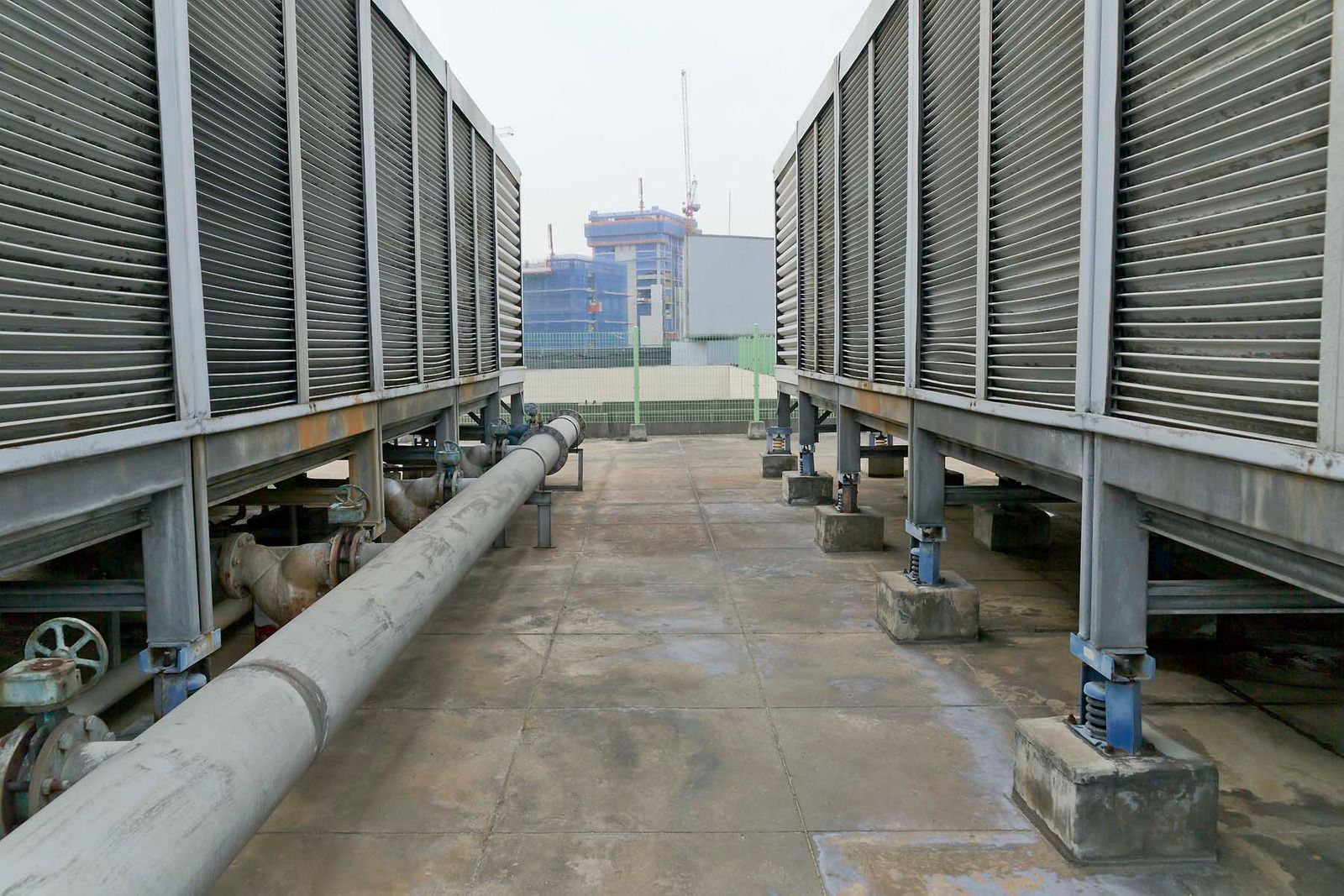 Industrial cooling towers with large pipes and a concrete walkway leading to a distant building.