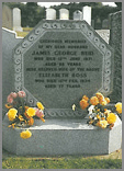 Octagonal shaped Dark Grey granite memorial with deep carved wave design, sitting on a splayed corner base with two flower containers.