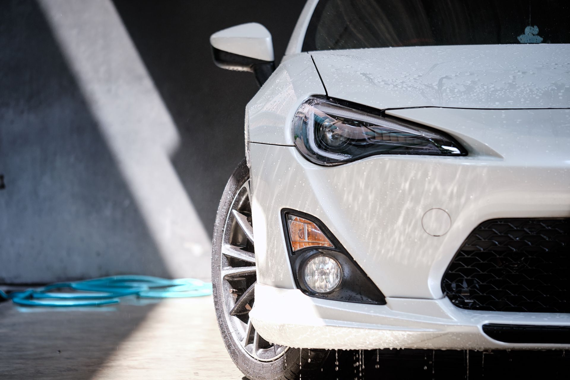 A white car is being washed with a hose in a garage.