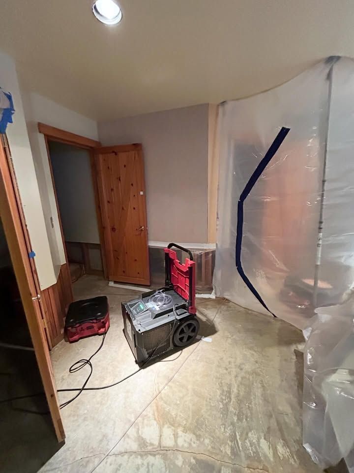 Partially finished room with a fan, tools, and plastic sheeting on the wall and floor