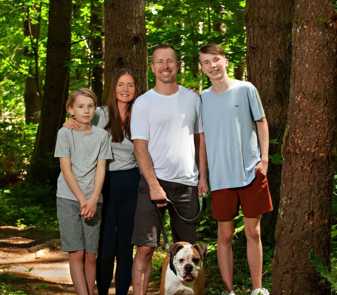 Four people and a dog standing on a forest trail in dappled sunlight