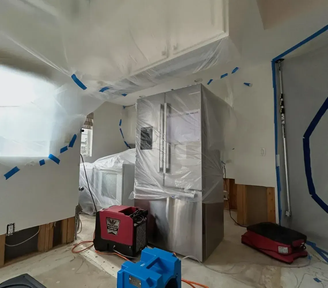 Plastic-covered interior with blue tape, a red tool cart, and a blue air scrubber during renovation work