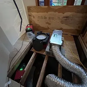Partially built floor vent with flexible ducts, a fan, and tools in a wooden-framed space