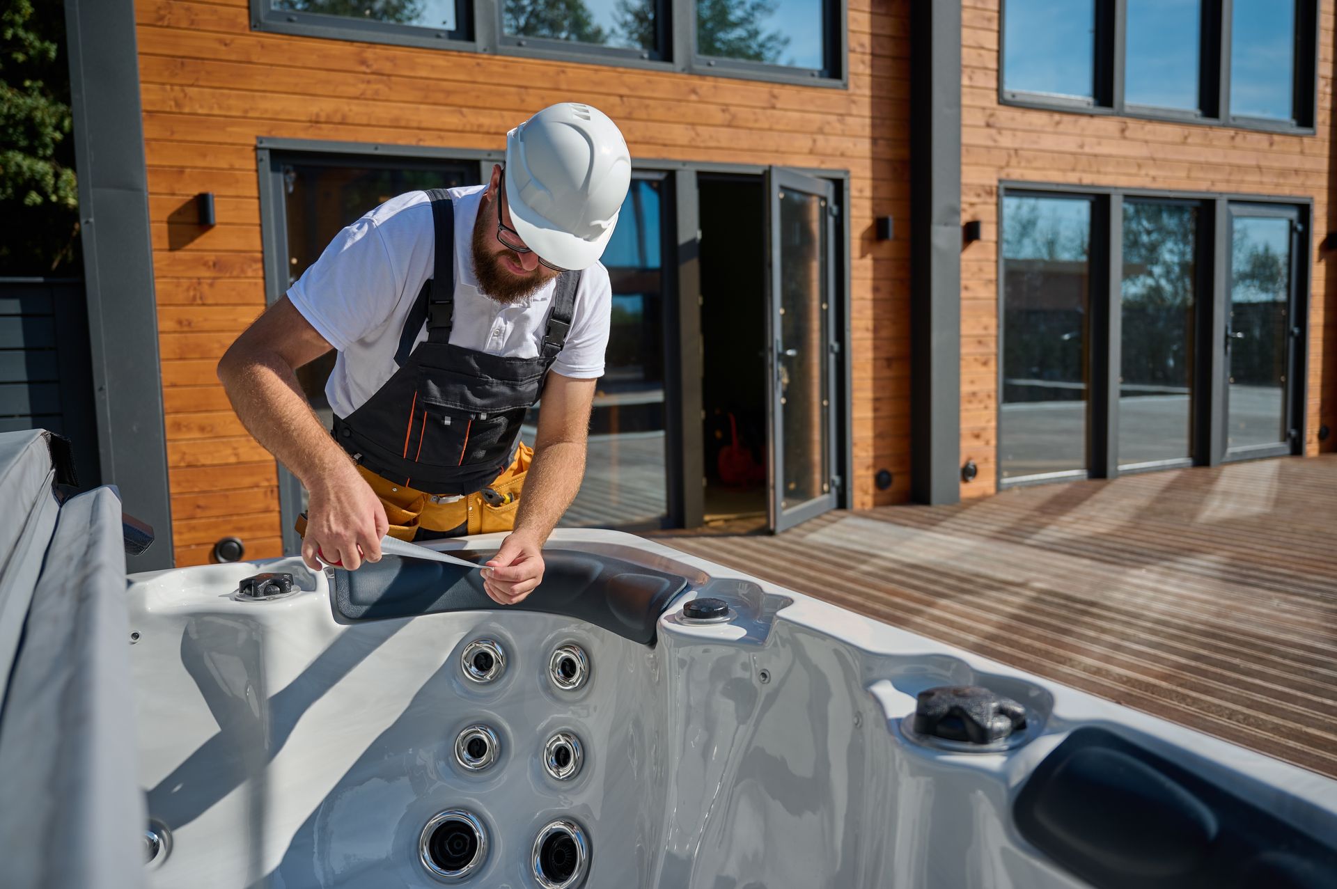 Worker installing fittings inside an outdoor hot tub beside a modern building