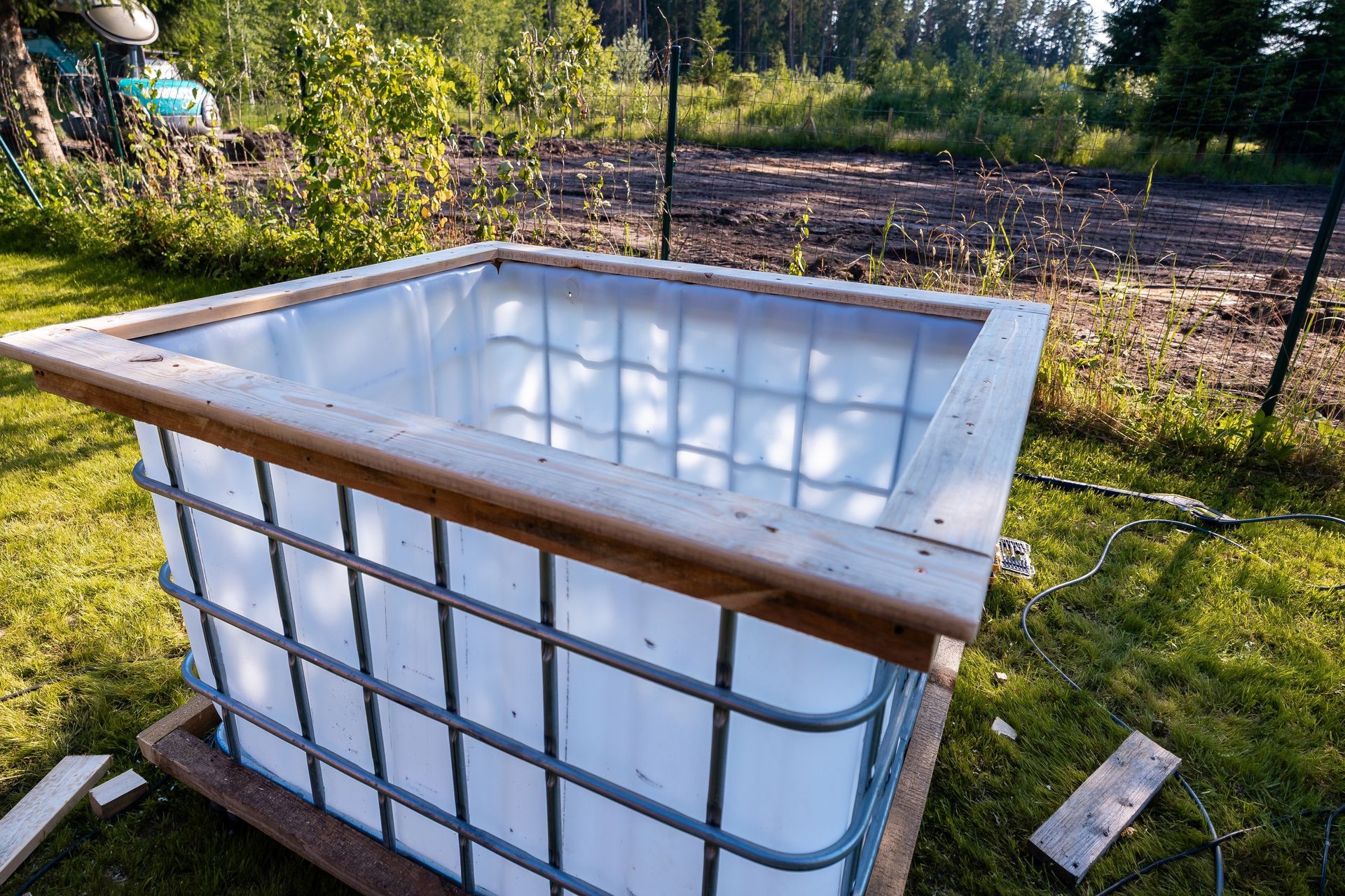 Wood-framed white IBC water tank in a sunny garden near a fenced field