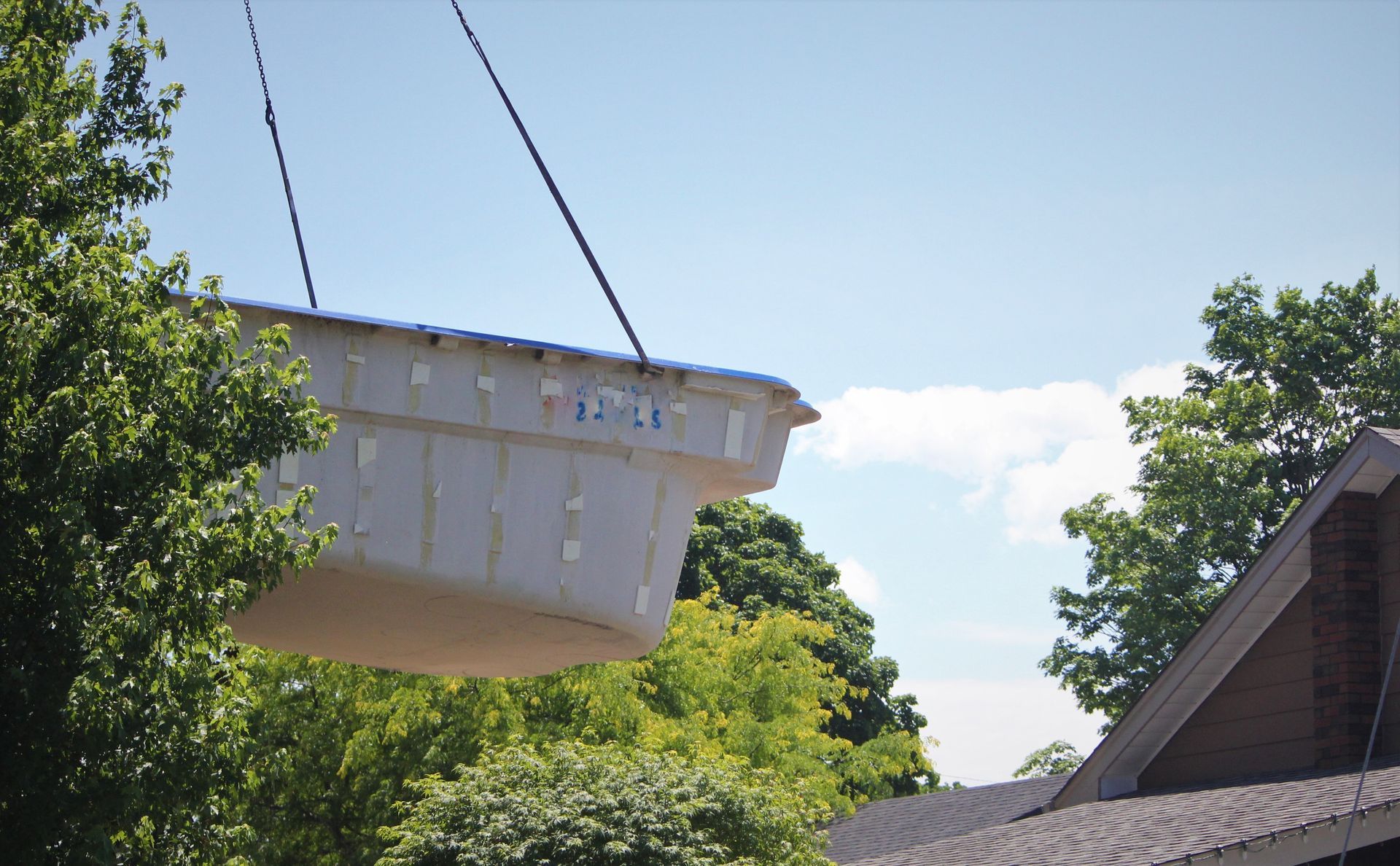 Large white suspended tank being lifted above trees and rooftops under a blue sky