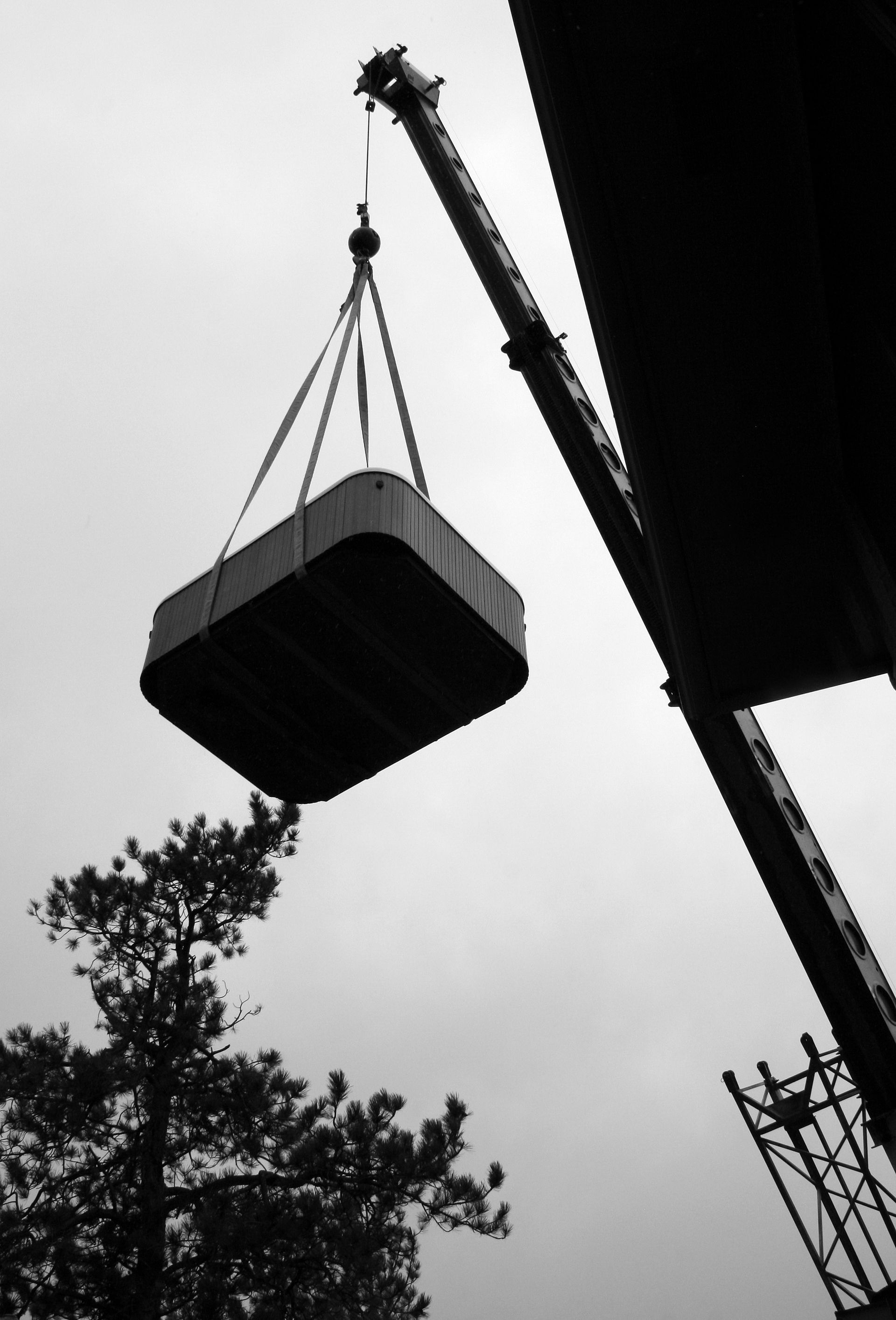 Crane lifting a large rectangular block above trees in a black-and-white scene