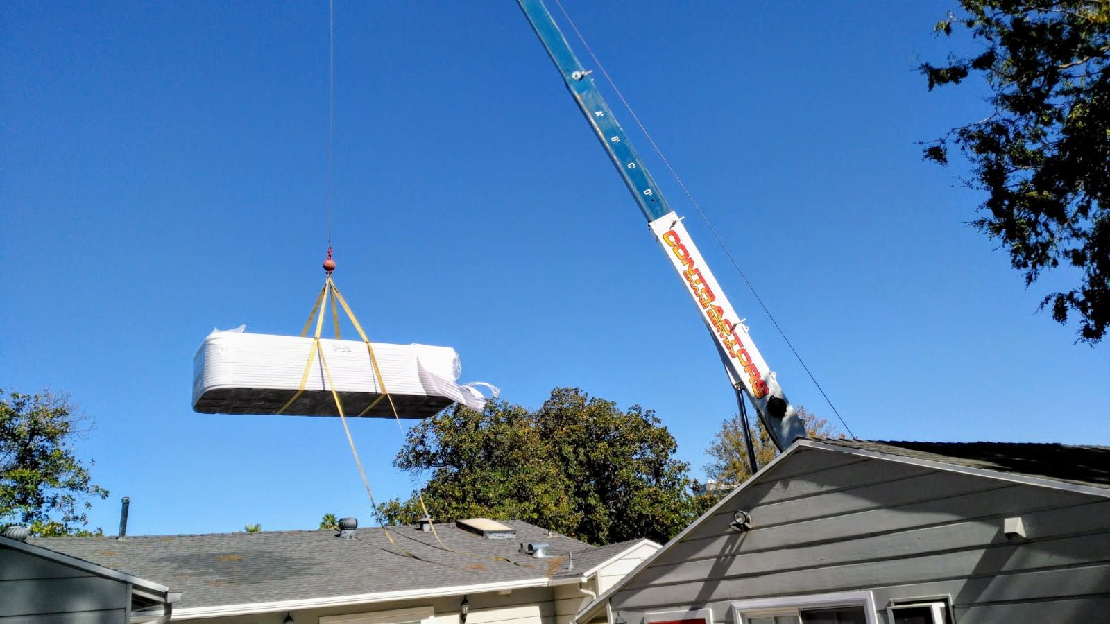 Crane lifting a large white bundle over rooftops under a blue sky.
