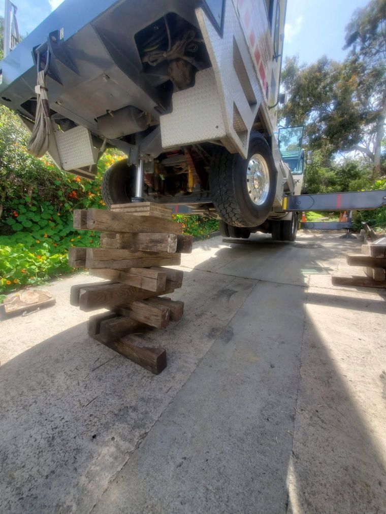 Raised vehicle supported by stacked wooden blocks on a driveway, with a wheel partly visible.