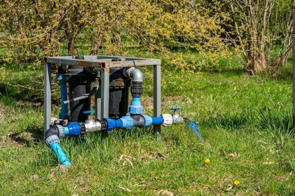 Blue irrigation pipes and valves on a metal frame in a grassy field near trees