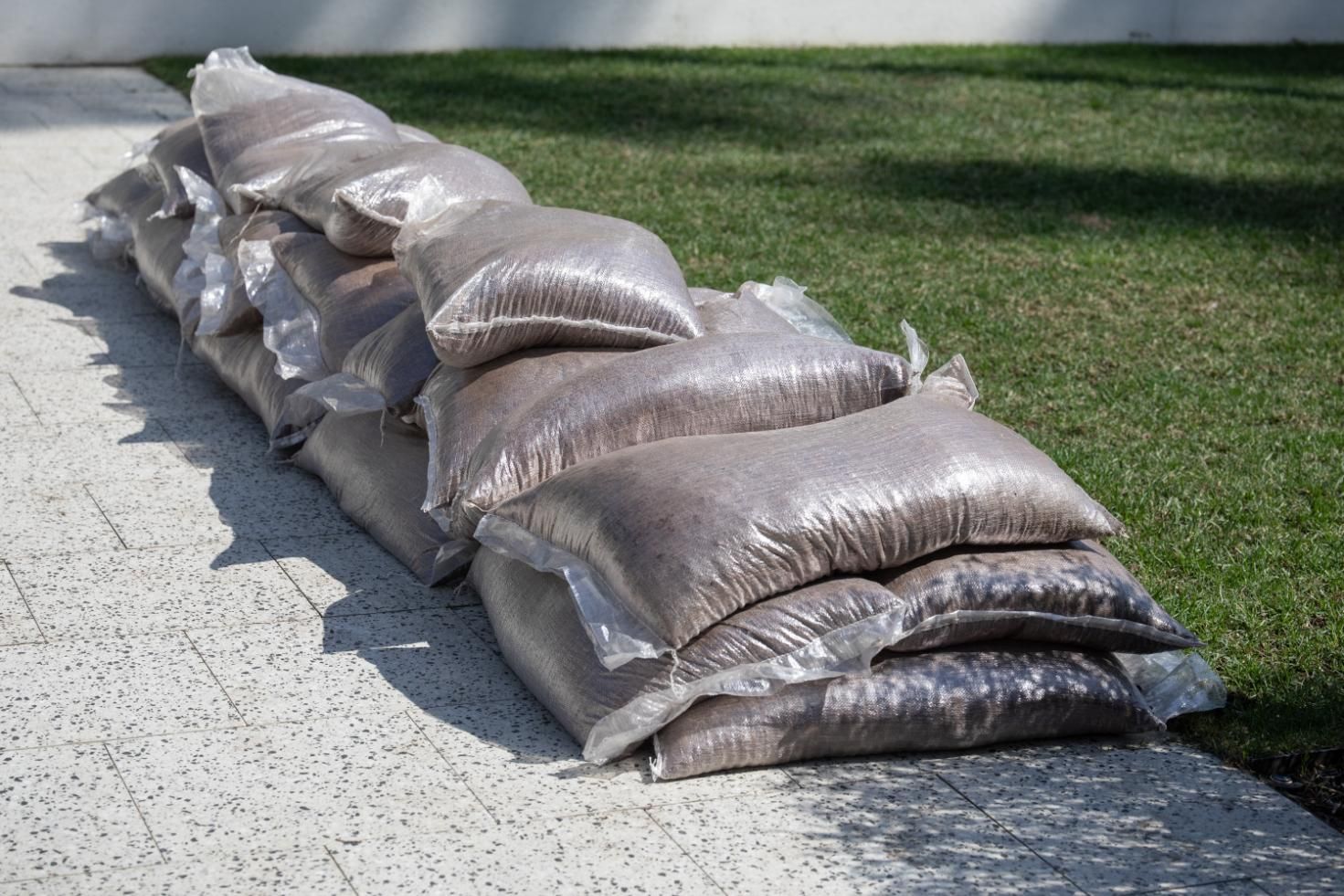 Stack of sandbags lining a curb beside a grassy lawn and concrete walkway