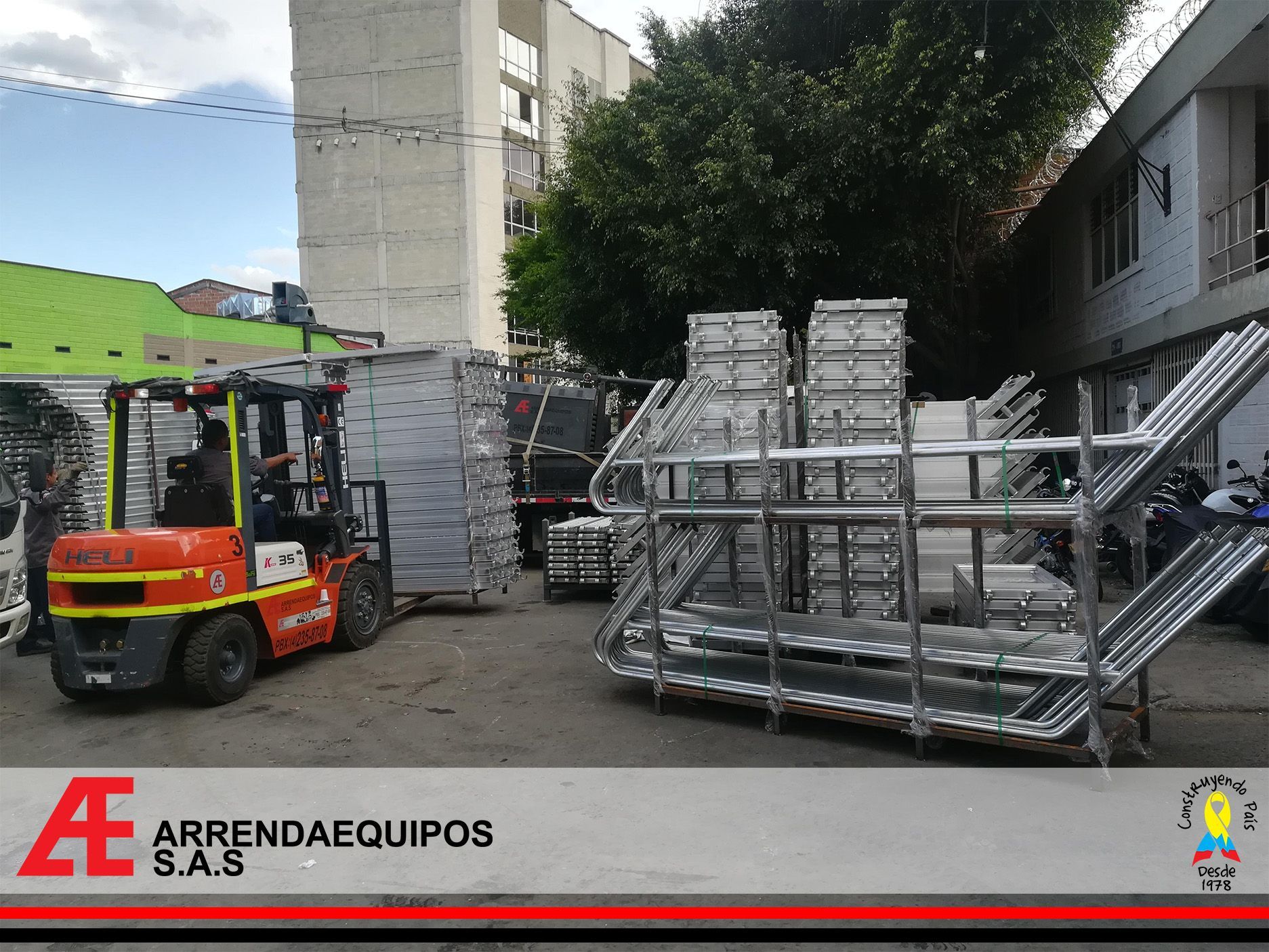 Carretilla elevadora moviendo andamios metálicos al aire libre, cerca de un edificio.