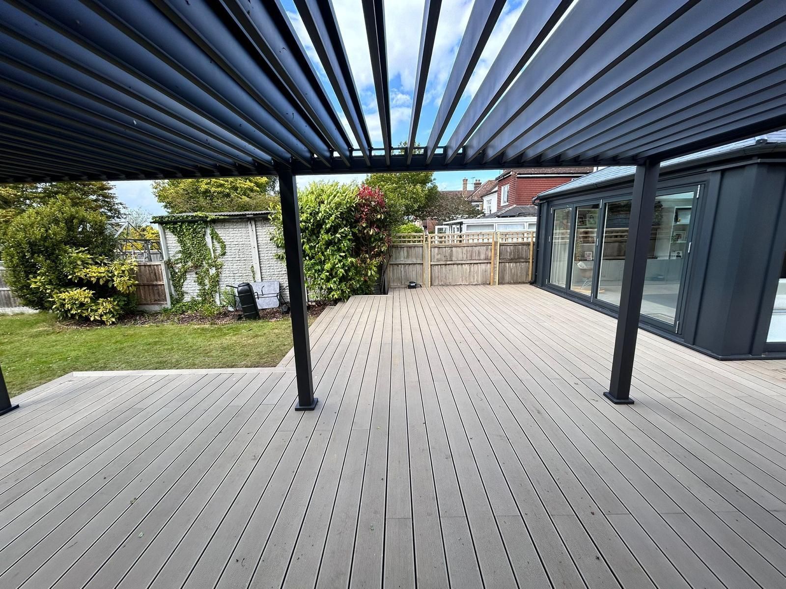 Covered wooden deck with pergola, black posts, and a yard view through glass doors.