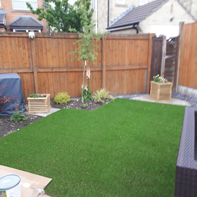 Backyard with fresh green lawn, wooden fence, and small planted border under a cloudy sky