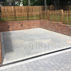 Empty paved patio with brick retaining walls and a wooden fence behind it