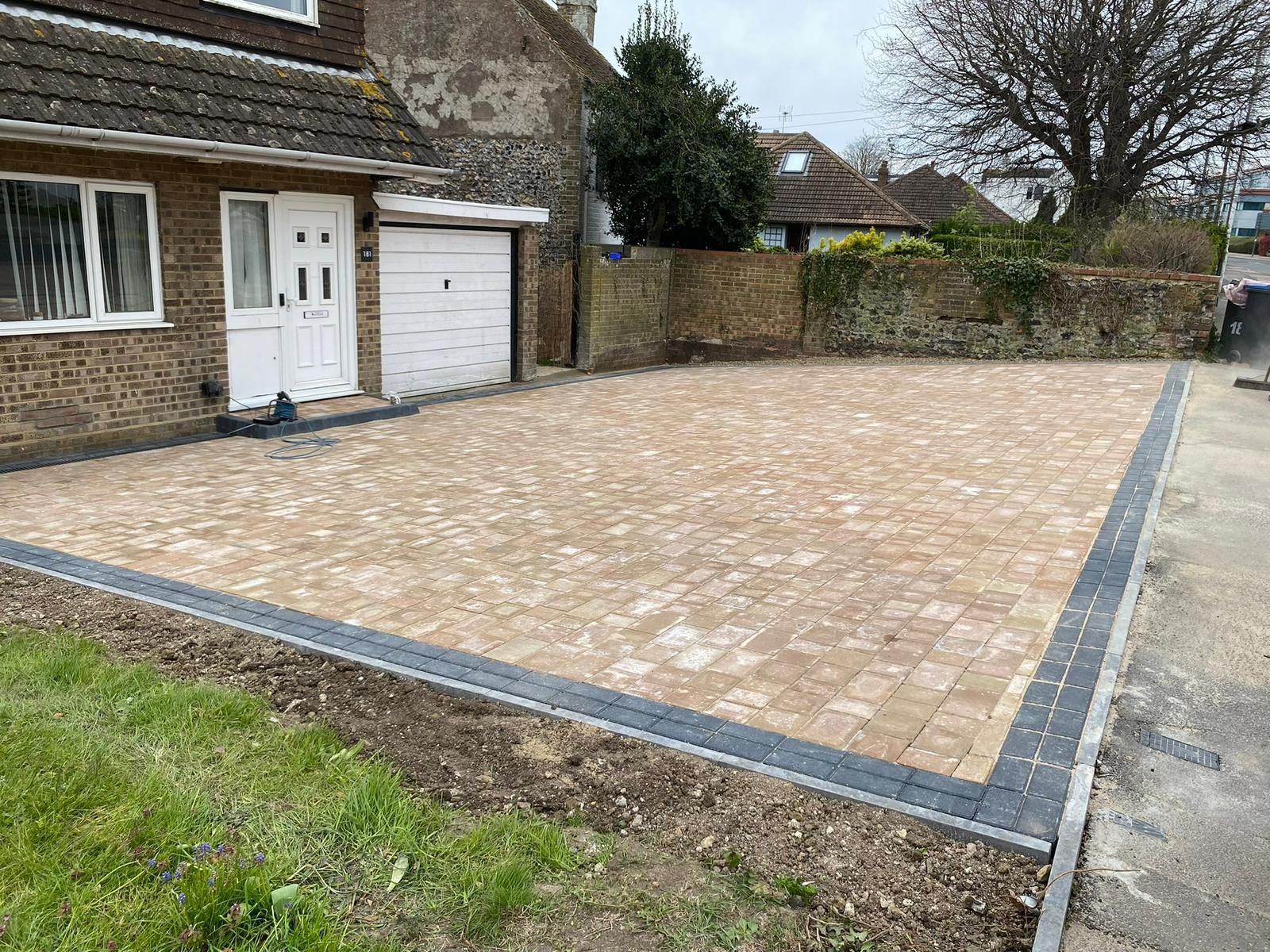 Brick-paved driveway beside a house and garage, bordered by stone edging and grass.