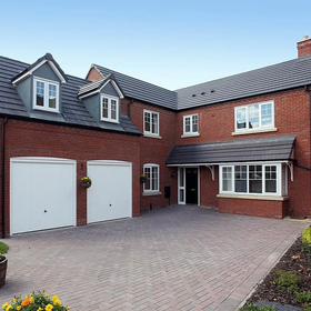 Brick house courtyard with double garage doors, a paved driveway, and a bay window.