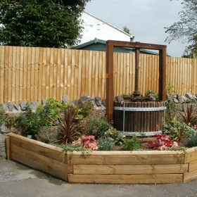 Raised flower bed with a wooden fountain in front of a vertical timber fence