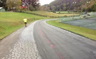 A person is walking down a road next to a tennis court.