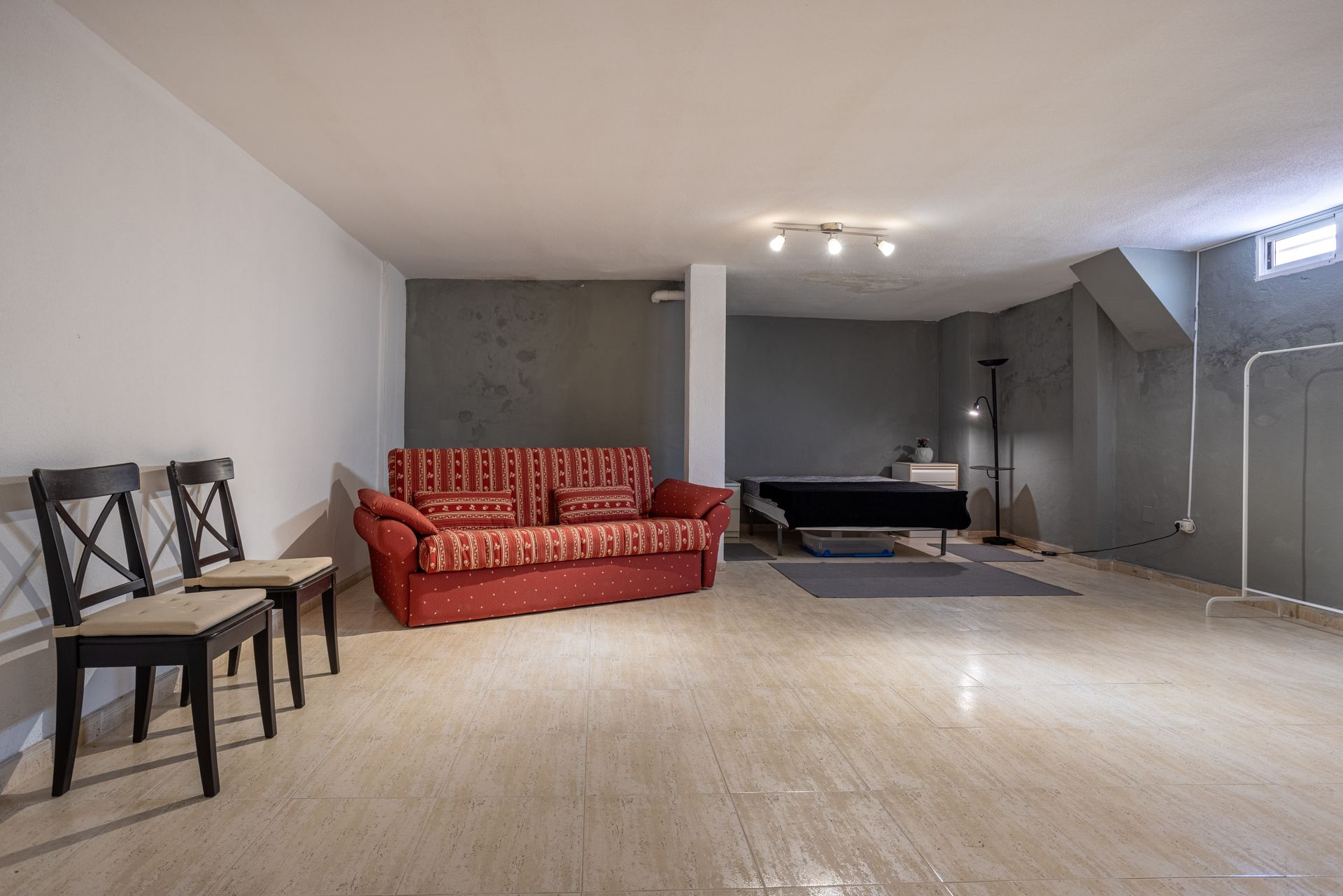 Spacious basement living room with red sofa, black chairs, and carpeted floor under recessed lighting