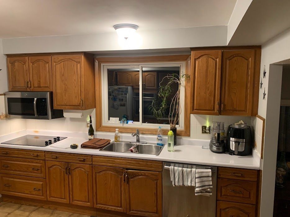 Modern kitchen with wooden cabinets, white counters, window over sink, and countertop appliances