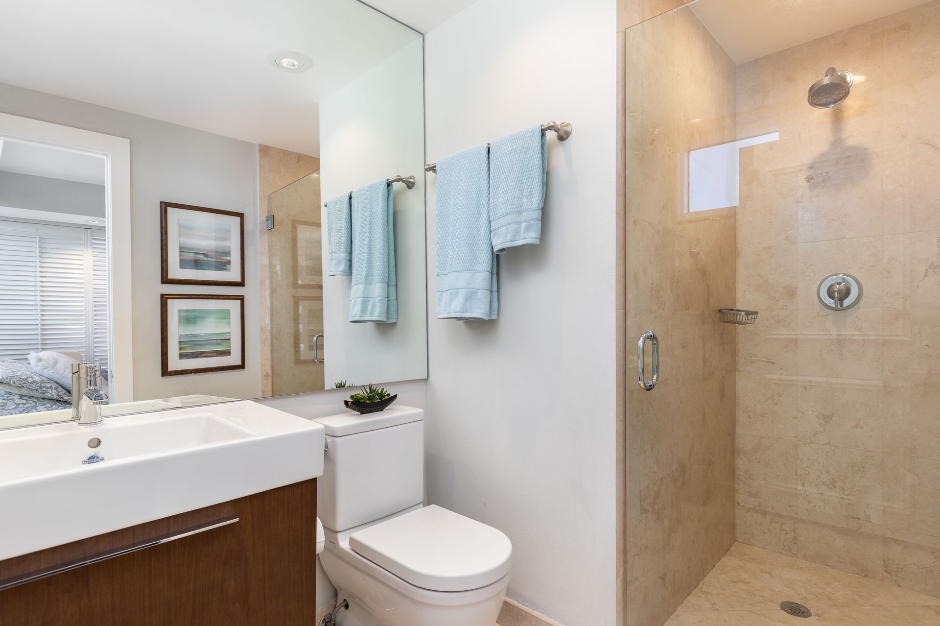 Modern bathroom with vanity, toilet, and glass shower with beige tile and blue towels