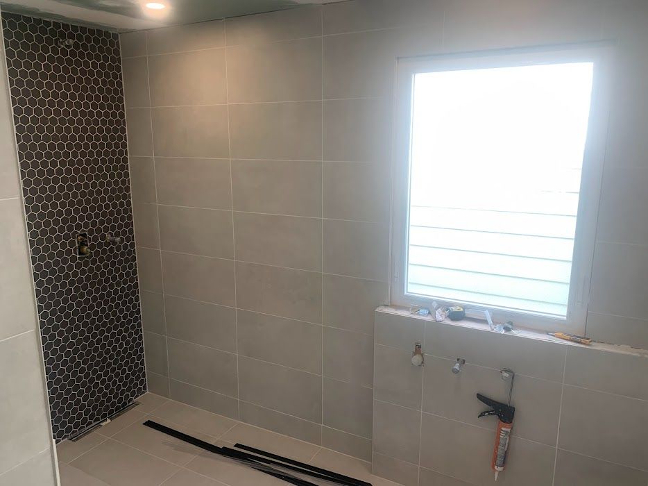 Bathroom with tiled walls, shower with dark mosaic tiles, window with white blinds.