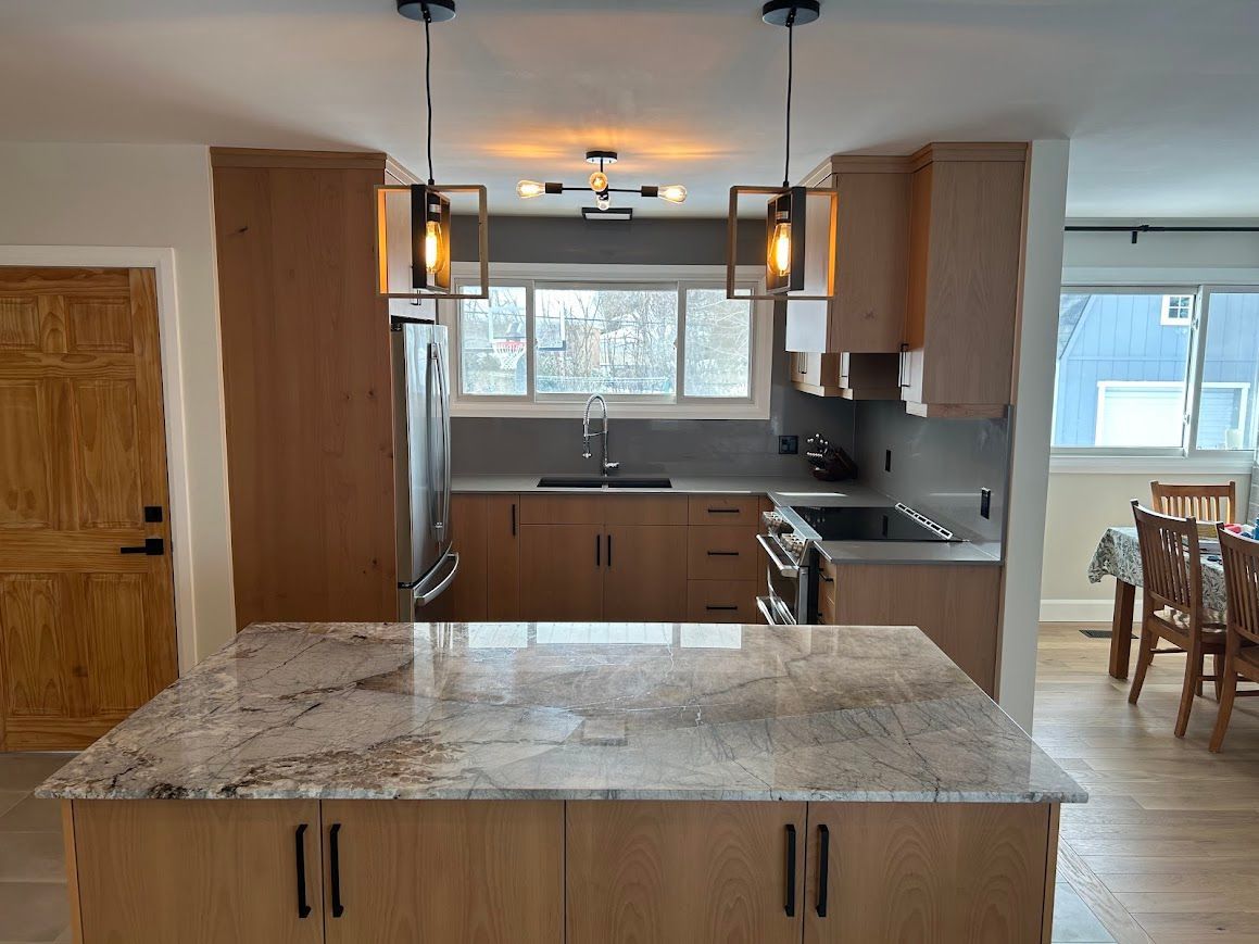 Modern kitchen with marble island, wood cabinets, pendant lights, and a dining area by the window