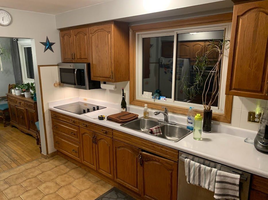 Kitchen with wooden cabinets, white countertops, sink by a window, and microwave above the stove.