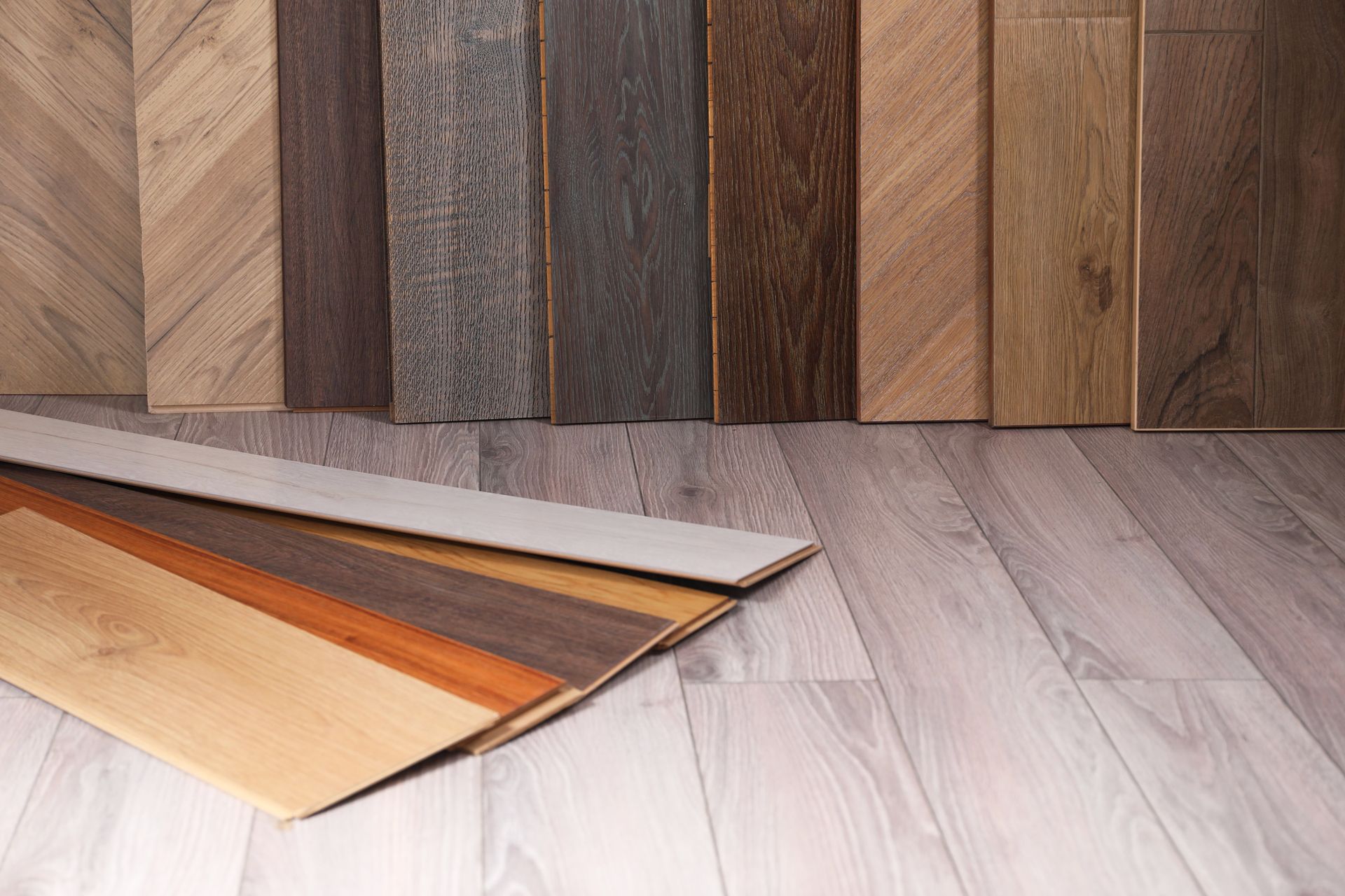 Wood flooring samples fanned out on a light gray wood floor against a backdrop of vertical wood planks