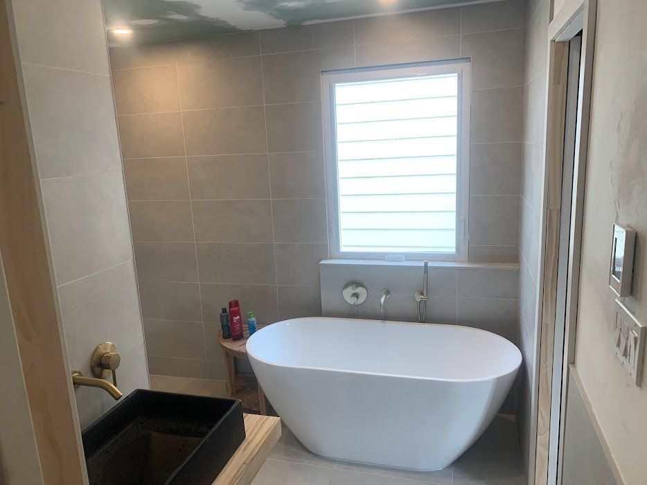 Modern bathroom with a freestanding white tub, tiled shower, and window above the faucet.