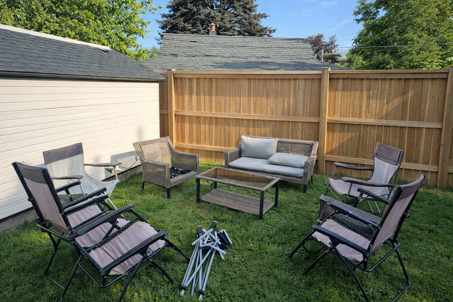 Patio with wicker furniture set, folding chairs, and wooden fence on a grassy lawn.
