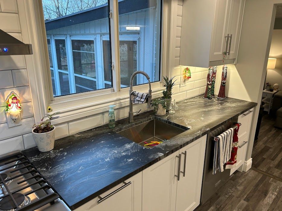 Modern kitchen counter with sink, stove, white cabinets, and large window above the countertop.