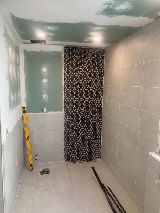 Bathroom under renovation, with gray tiling and a partially tiled accent wall. Drywall and tools visible.