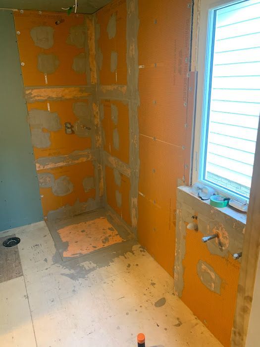 Shower construction in progress: orange waterproof board walls, gray mortar, window.
