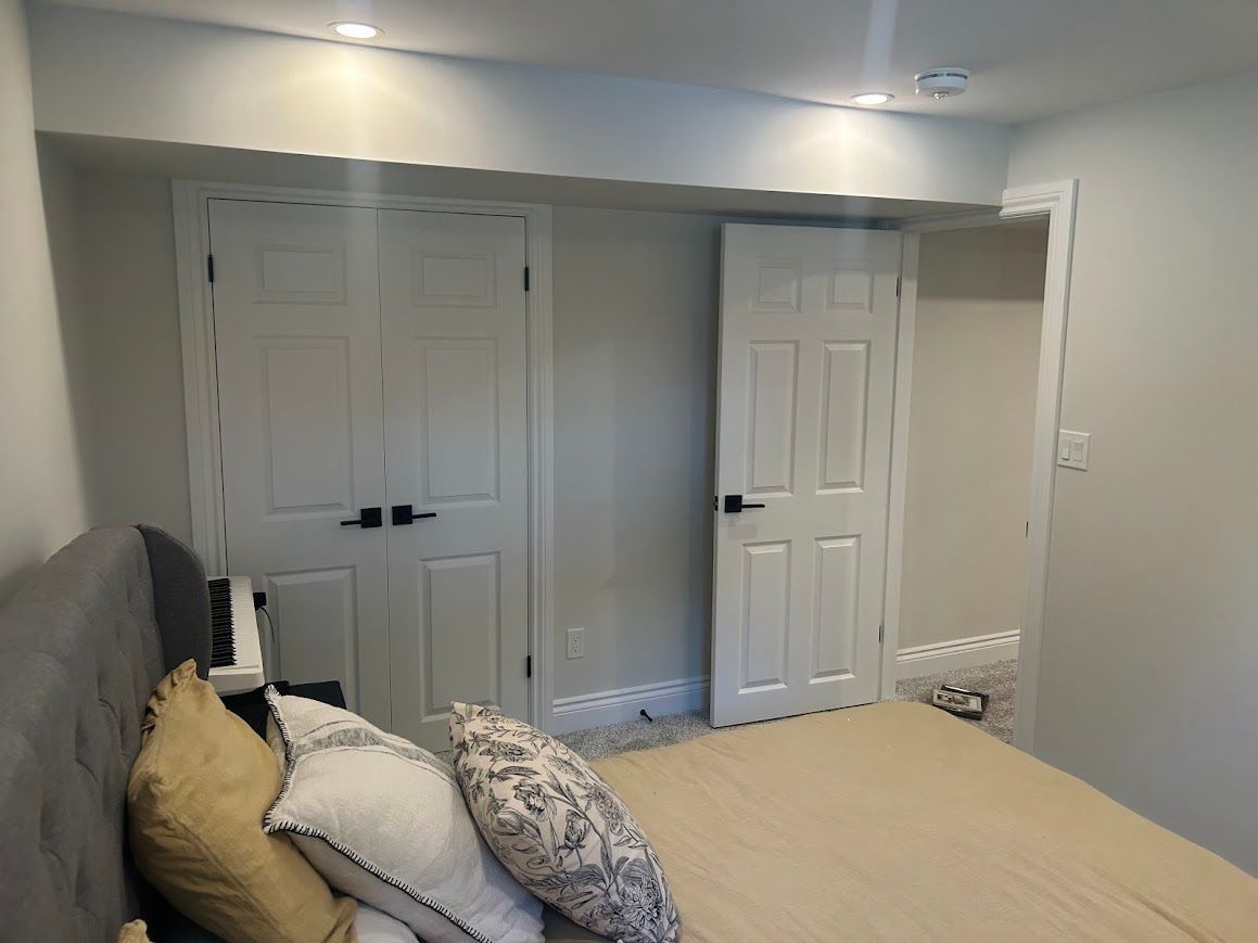 Bedroom with white doors, gray walls, bed with pillows, and recessed lighting.