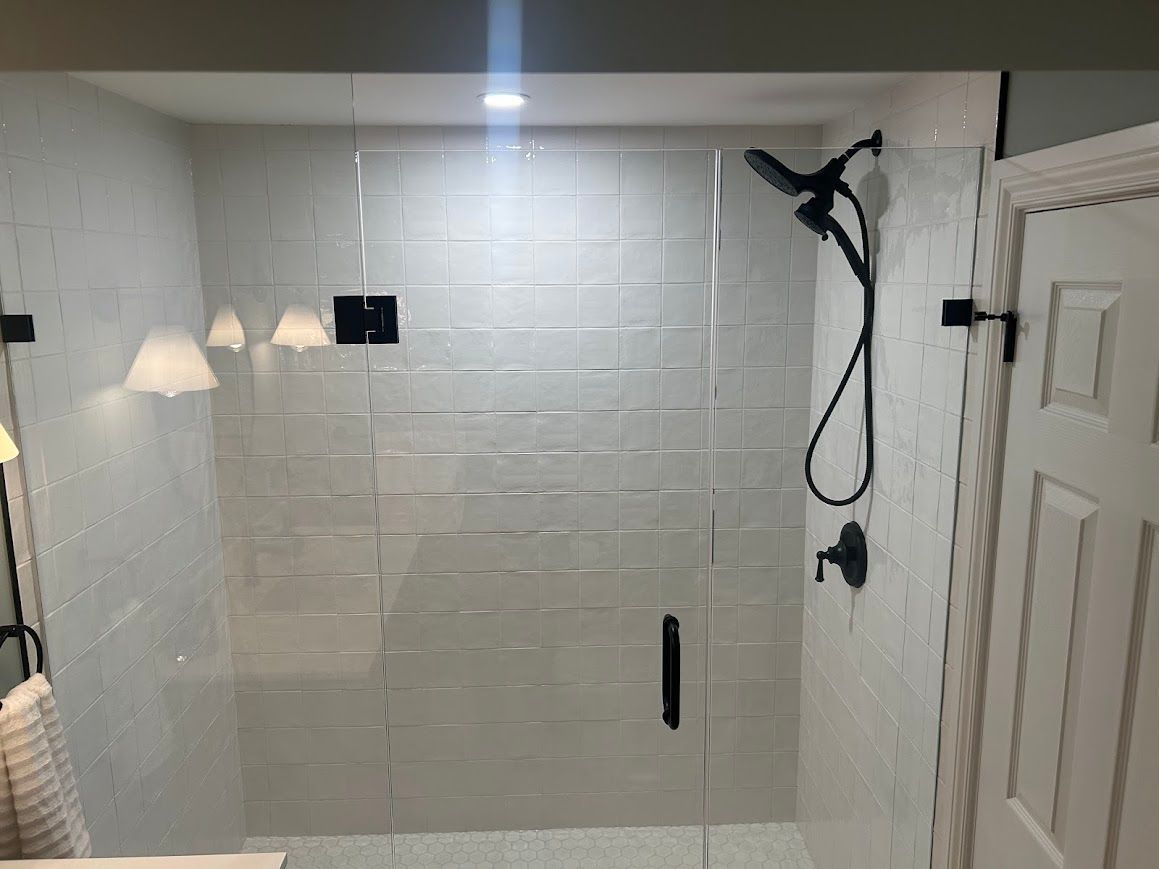 Modern bathroom with white subway tile shower, glass door, black fixtures, and sconces.
