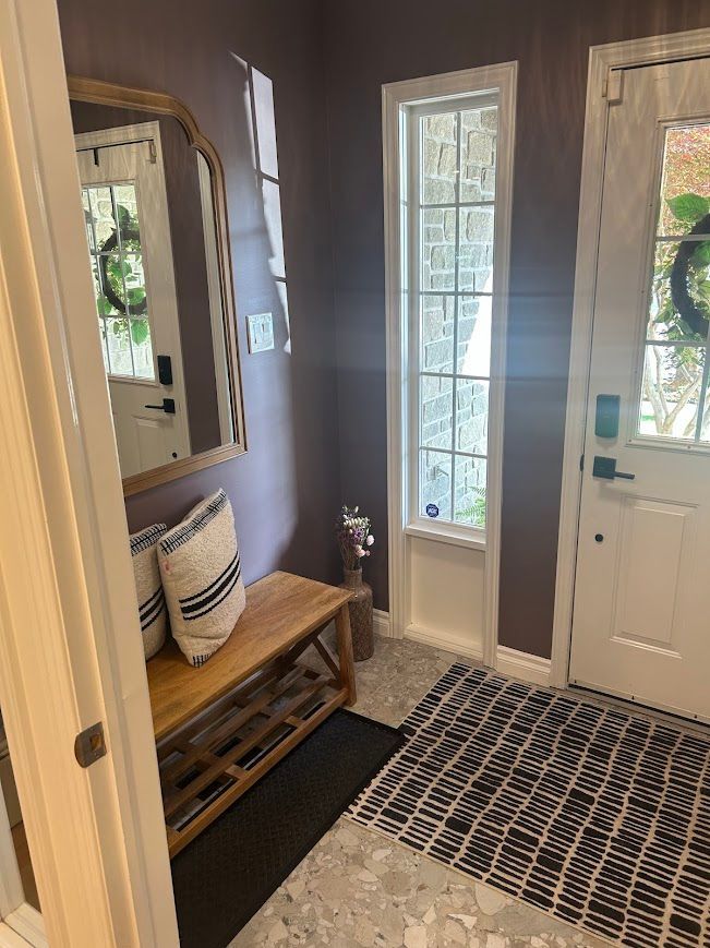 Entryway with bench, mirror, dark gray walls, white trim, and a patterned rug.