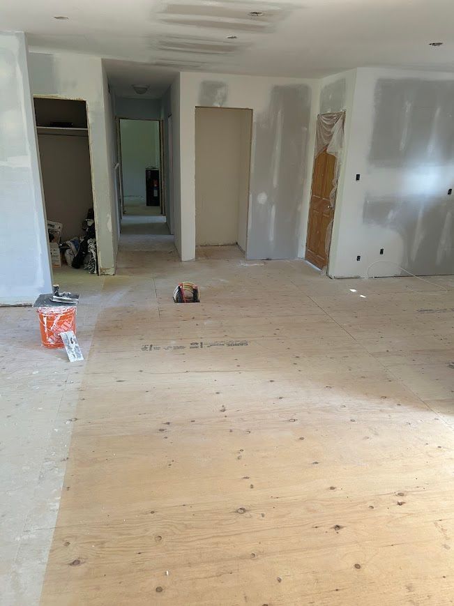 A room under renovation with plywood flooring, partially finished drywall, and doorways leading to other areas.