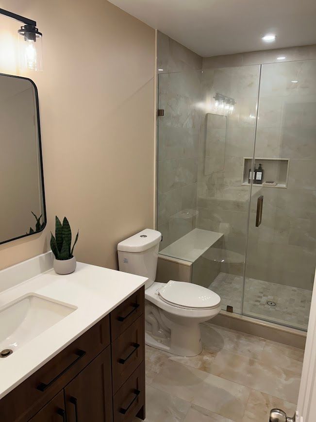 Modern bathroom with white countertops, brown cabinets, glass shower, and beige walls.