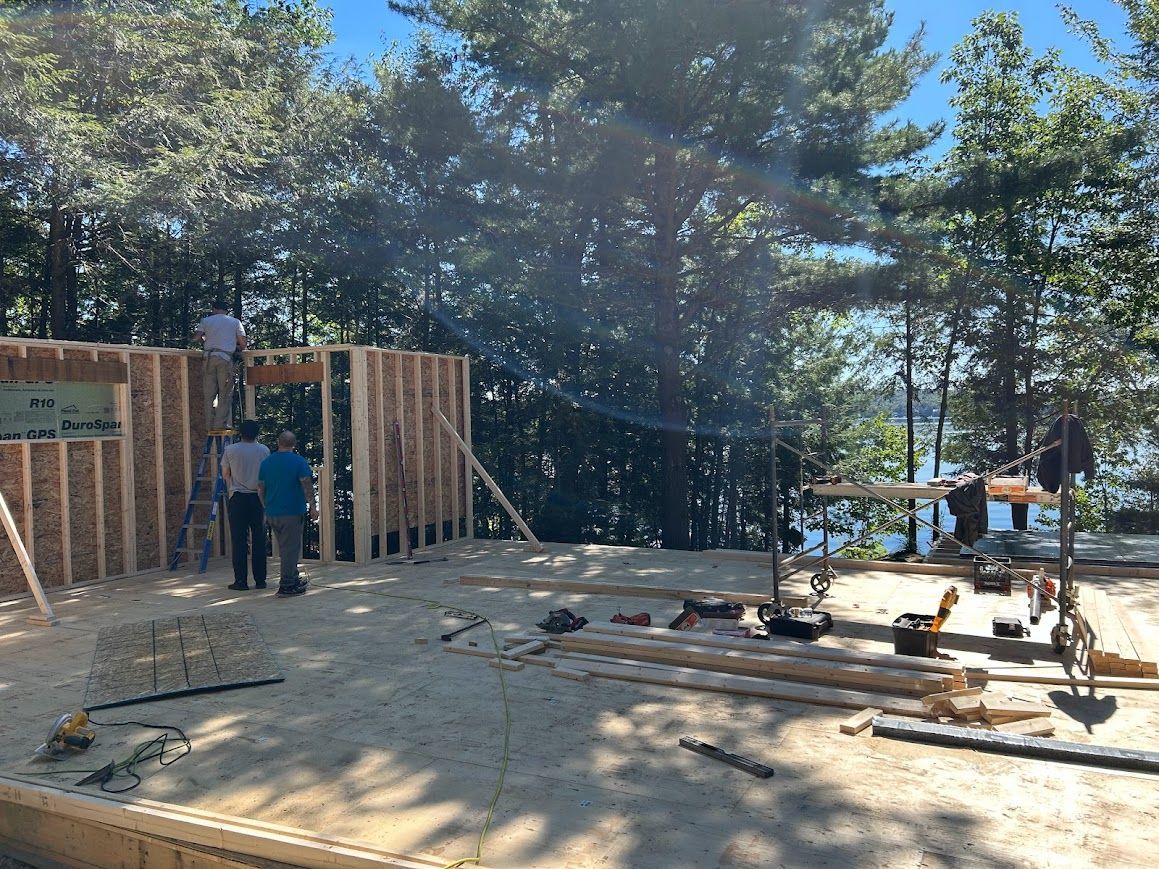 Construction of a wooden framed building with workers, tools, and a lake view.