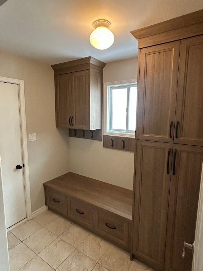Laundry room with wood cabinets, bench, and window. Beige walls and tiled floor.
