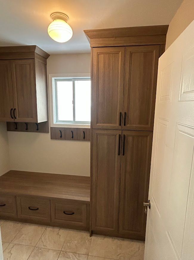 Mudroom with wood cabinets, bench, hooks, and a window.