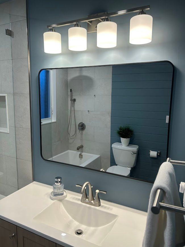 Bathroom with blue walls, a rectangular mirror, a white sink, and a four-light fixture.
