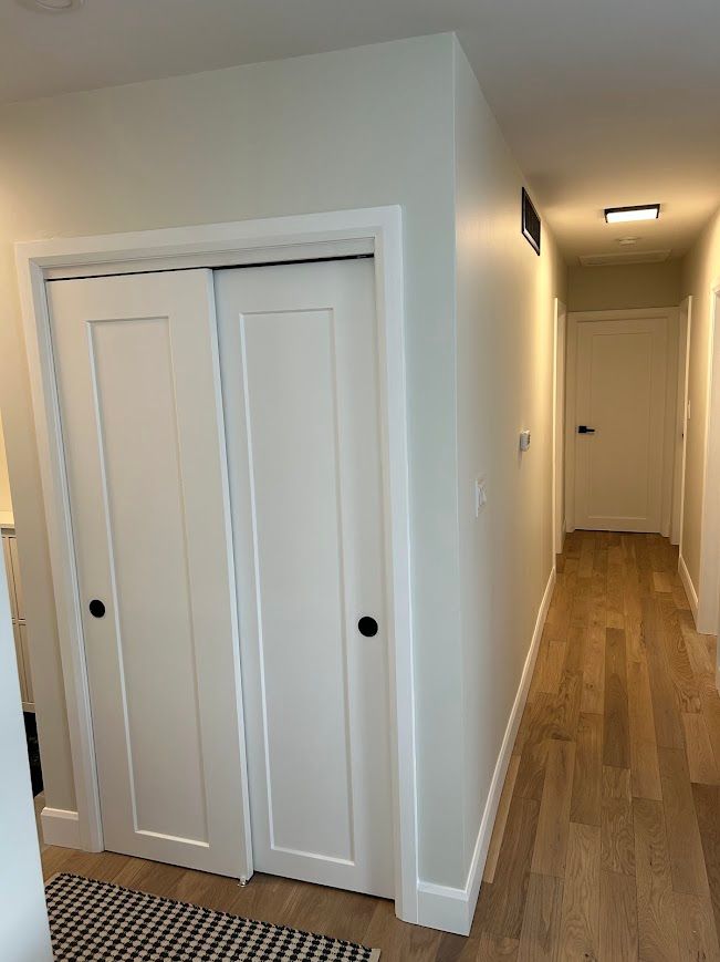 Hallway with closet. White doors, light wood floors, and white walls.