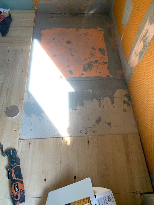 Shower base under construction with orange waterproofing membrane, plywood floor, and tools.